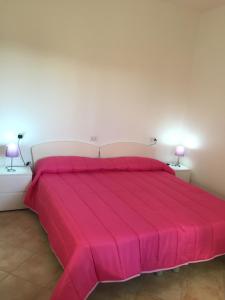 een groot roze bed in een witte kamer met 2 lampen bij Ginepro family in Valledoria