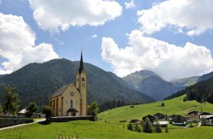a church in a field with mountains in the background at Aparthotel B&B Monte in Kartitsch +92 photos