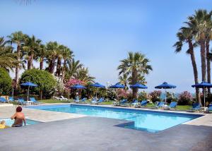 a woman standing next to a swimming pool with blue umbrellas at Rododafni Beach Apartments in Paphos