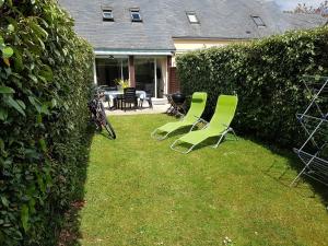 deux chaises vertes assises dans une cour à côté d'une haie dans l'établissement Marina Apartment, à La Forêt-Fouesnant
