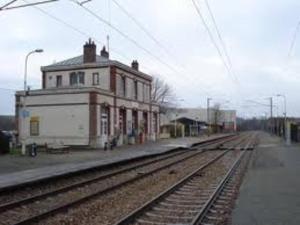 a train station with a building next to the tracks at Dépendance cosy dans le Vexin, terrasse et jardin in Us