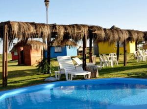 a swimming pool with chairs and a straw umbrella at Termas Sol Y Luna con AGUA TERMAL in Termas del Daymán