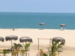 una playa con algunas sombrillas de paja y el océano en Palmeras de Bocapan, Tumbes, en Zorritos