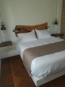 een groot bed met witte lakens en een houten hoofdeinde bij Casa del Sol in Villa de Leyva