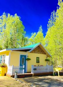 a small yellow and blue house with a white fence at Sunshine Cottage in Talkeetna