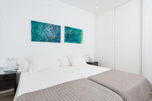 a white bedroom with a bed and two paintings on the wall at Mirador Blue D - Cala Sant Vicenç in Cala de Sant Vicenc