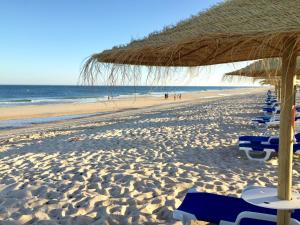 a beach with chairs and a straw umbrella and the ocean at Quinta da Lua in Tavira