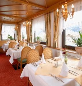 un restaurante con mesas y sillas blancas y ventanas en Hotel Edelweiss, en Pfunds