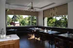 a dining room with tables and chairs and large windows at Mastiff Villa Camellia by OTHPL in Pālampur