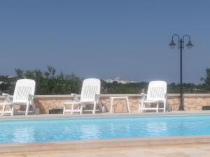 a group of white chairs sitting next to a swimming pool at Trulli Dal Conte in Locorotondo