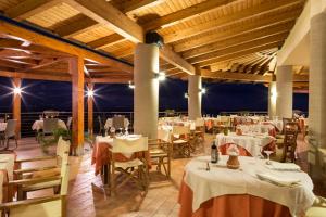 un restaurante con mesas blancas, sillas y luces en Hotel Santa Chiara, en Capo Vaticano
