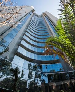 un edificio alto con ventanas de cristal y palmeras en Apartamento Alphaville - Barueri/SP, en Barueri