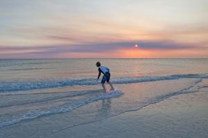 a man walking in the water on the beach at Inn at Pelican Bay in Naples