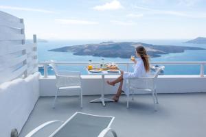 Eine Frau, die an einem Tisch auf einem Balkon sitzt und Essen isst. in der Unterkunft Asma Suites in Fira