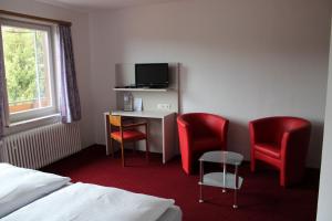 バート・グルントにあるHotel-Pension Waldhausのデスクと赤い椅子2脚が備わるホテルルームです。