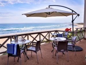 zwei Tische und Stühle unter einem Sonnenschirm am Strand in der Unterkunft On the Beach Guesthouse Jeffreys Bay in Jeffreys Bay