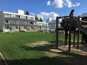 Uma rapariga está sentada num parque infantil em frente a um edifício. em Ferienwohnung Marion em Sankt Englmar