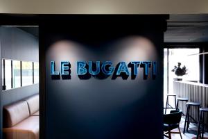 ein blaues Schild mit der Aufschrift „le buattestation“ an einer Wand in der Unterkunft Hotel Le Bugatti in Molsheim