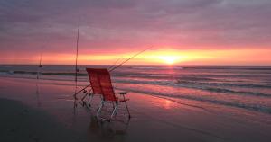 a chair sitting on the beach watching the sunset at Finistère in Oosterend