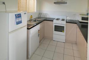 a kitchen with a white refrigerator and a sink at Tradewinds McLeod Holiday Apartments in Cairns