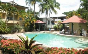 a swimming pool in front of a building with palm trees at Tradewinds McLeod Holiday Apartments in Cairns