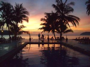 zwei Personen stehen in der Nähe eines Swimmingpools mit Palmen in der Unterkunft Frangipani Langkawi Resort in Pantai Cenang