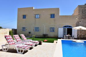a group of chairs sitting next to a swimming pool at Four Winds Farmhouse in Birżebbuġa
