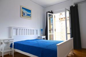 a white bedroom with a blue bed and a window at Old Town Apartment next to Seafront Promenade in Nafplio