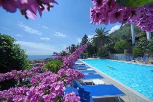 a pool with blue benches and purple flowers at Hotel Palazzina in Gargnano