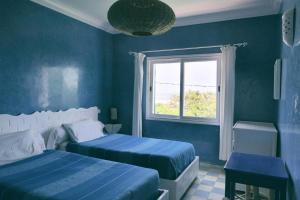 a blue bedroom with two beds and a window at Blue Kaouki in Sidi Kaouki