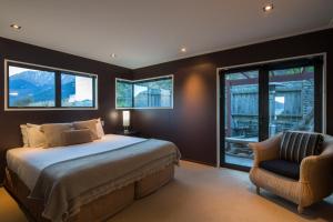 a bedroom with a bed and a chair and windows at Majestic View Home in Queenstown