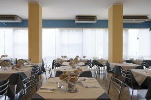 uma sala de jantar com mesas, cadeiras e janelas em Hotel Rondinella em Cesenatico