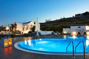 a large pool with chairs and a house in the background at Golden East in Imerovigli