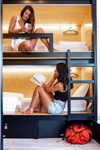 two women sitting on bunk beds talking on the phone at GiG Capsule Hostel in Ericeira
