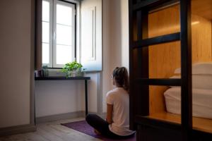 a woman sitting on the floor next to a bunk bed at GiG Capsule Hostel in Ericeira