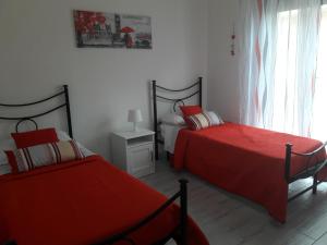 two beds in a bedroom with red sheets at Apartaments "Le vele 1" in Pachino