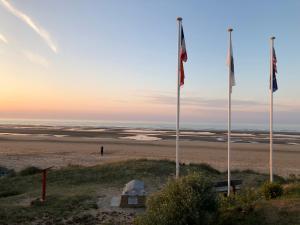 two flags on a beach with a man standing on the sand at Villa kahlo Omaha Beach in Colleville-sur-Mer
