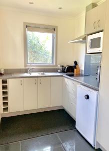 uma cozinha com armários brancos, um lavatório e uma janela em Mirror Creek Holiday Cottage em Ruatapu