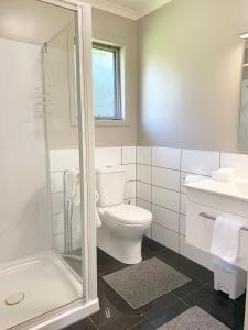 La salle de bains blanche est pourvue d'une douche et de toilettes. dans l'établissement Mirror Creek Holiday Cottage, à Ruatapu