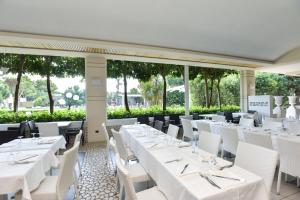 um restaurante com mesas brancas, cadeiras brancas e janelas em Hotel Club Astor em Ugento