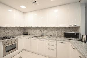 a white kitchen with white cabinets and a microwave at KeyHost - Spacious 1BR with Parking near Five hotel in JVC - Dubai - KG10 in Dubai