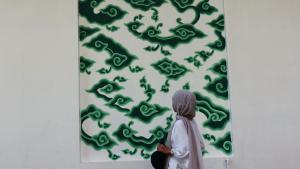a woman looking at a green painting on a wall at Metland Hotel Cirebon by Horison in Cirebon