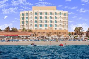 een groot gebouw aan het strand met een strand met een boot in het water bij Sharjah Carlton Hotel in Sharjah
