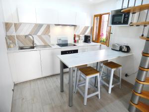 una cocina con armarios blancos, mesa y taburetes en Le Pouffre, maison de pêcheur au quartier des artistes, clim, WiFi, en Sète