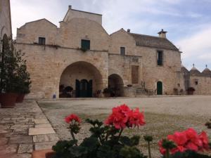- un grand bâtiment en pierre avec des fleurs rouges devant dans l'établissement Masseria Sant'Elia, à Martina Franca