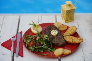 a red plate of food with a steak and salad at Vasilaras Hotel in Skala
