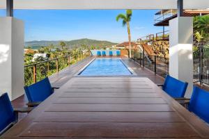 a long wooden table with blue chairs and a swimming pool at Nautilus On The Hill - Airlie Beach in Airlie Beach