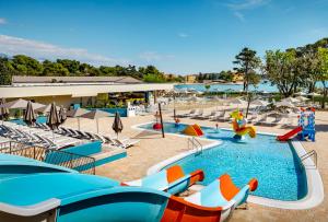 a pool with chairs, tables, and umbrellas at Padova Premium Camping Resort by Valamar in Rab