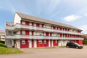 un bâtiment rouge avec une voiture garée dans un parking dans l'établissement Kyriad Rouen Sud - Oissel, à Saint-Étienne-du-Rouvray