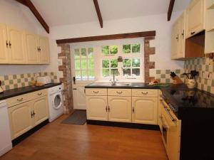 una cocina con armarios blancos, lavadora y fregadero en Dairy Cottage en Bodmin